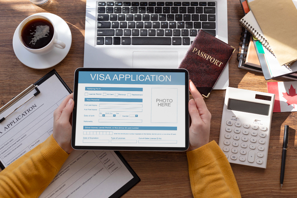 Top-down view of a student filling out a digital visa application on a tablet with a passport and Canadian flag on a wooden desk.